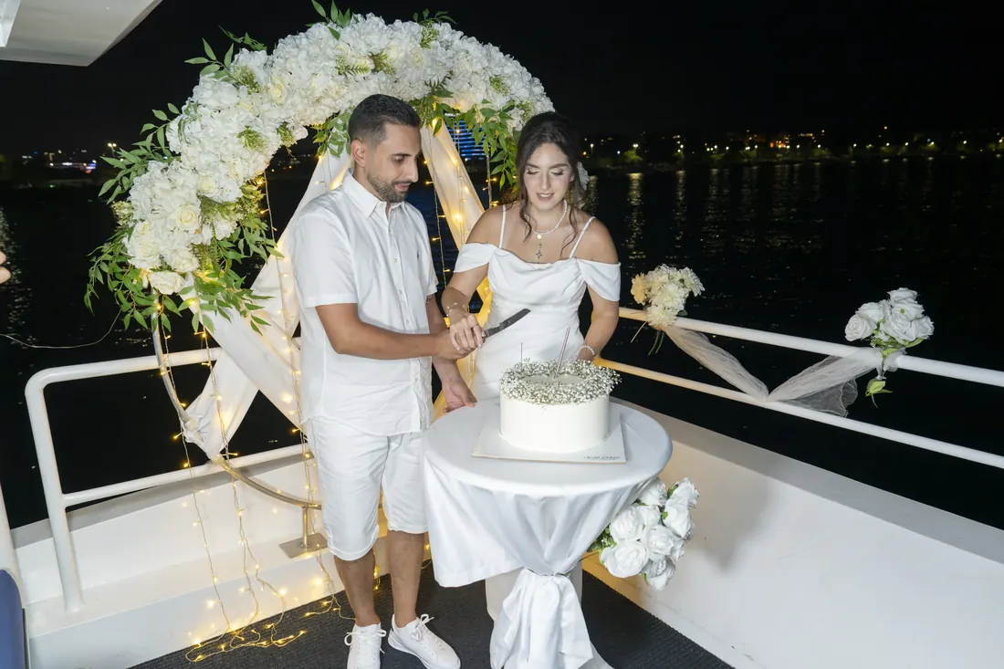Couple with a cake under a flower arch on a yacht