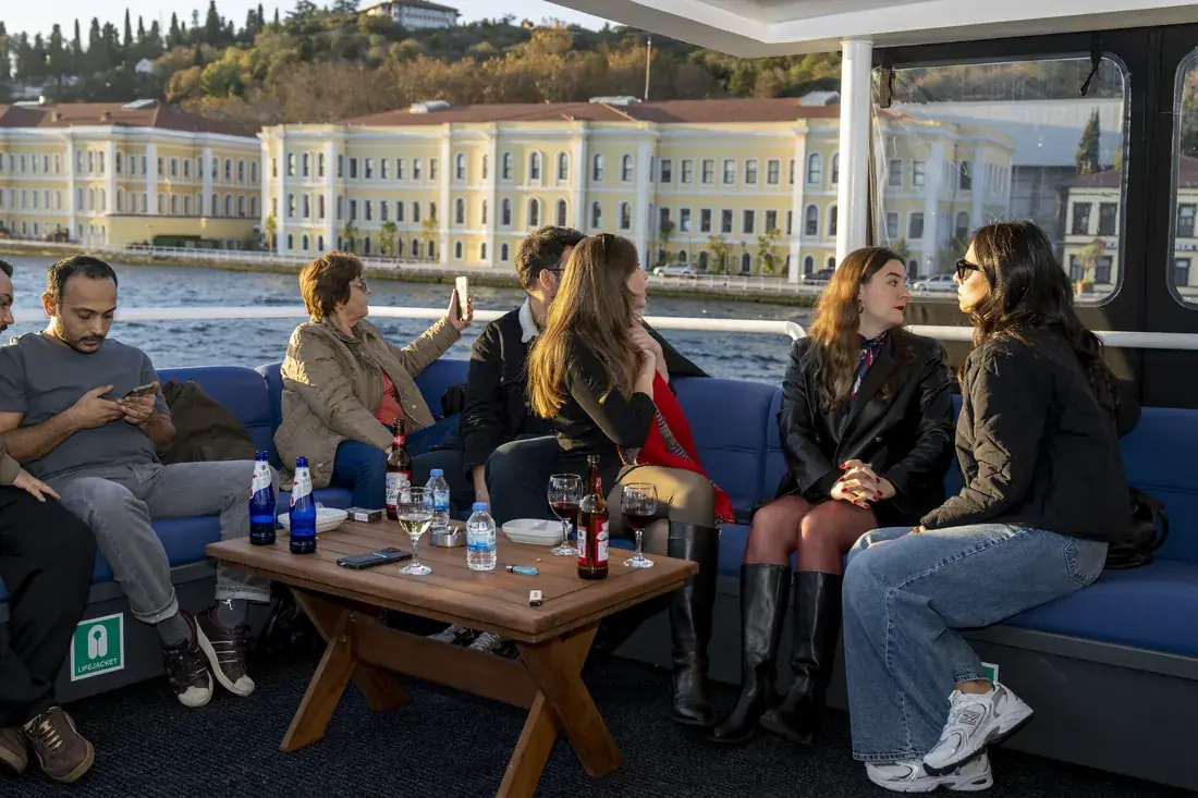 Invitados relajándose en el salón de un yate con un palacio junto al agua al fondo