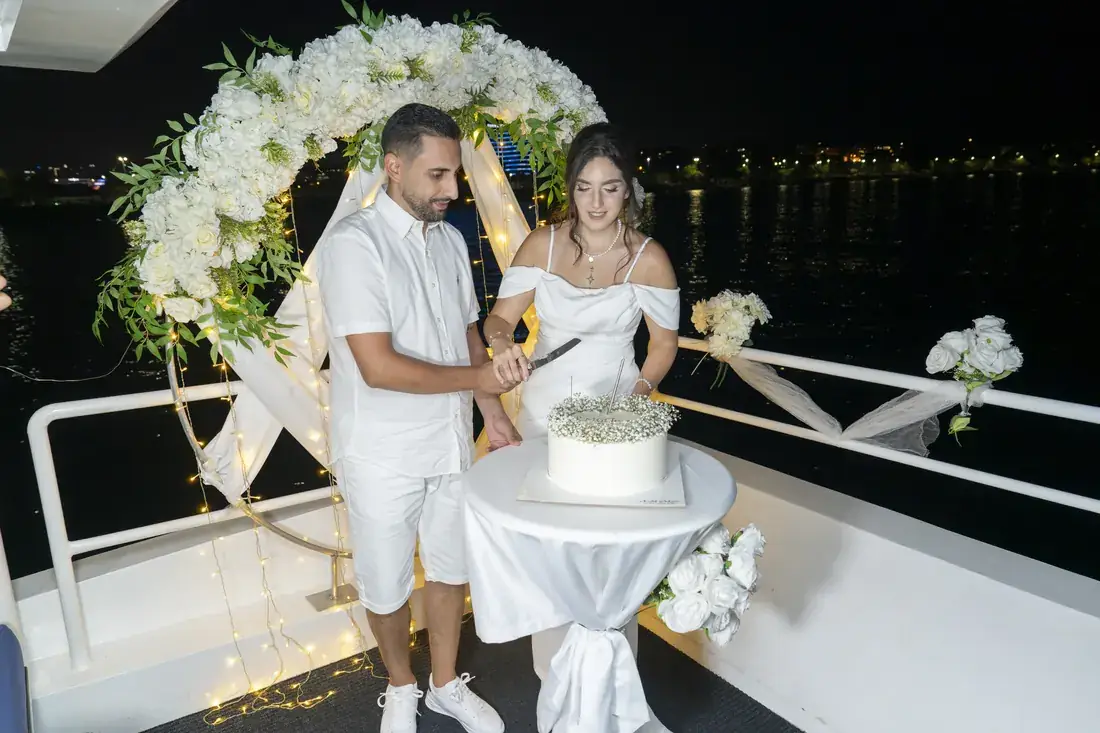 Newlyweds cutting the cake under a flower arch on a yacht