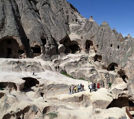 Hiking path through the green Ihlara Valley with rock walls and cave openings, Cappadocia